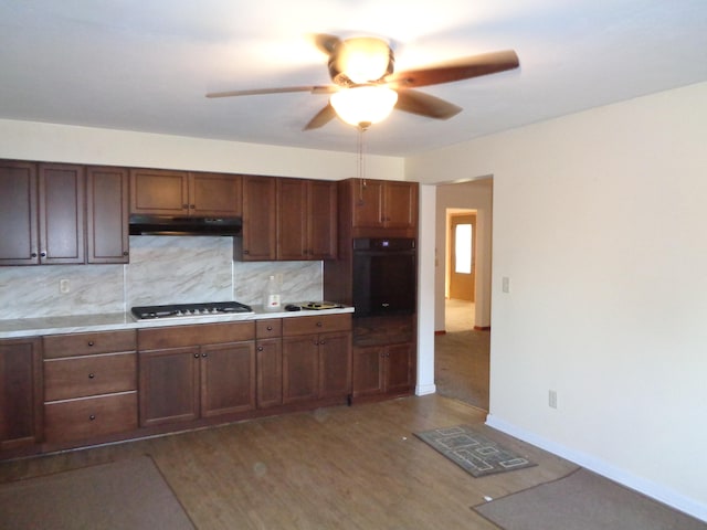 kitchen featuring stainless steel gas stovetop, decorative backsplash, dark hardwood / wood-style floors, ceiling fan, and black oven