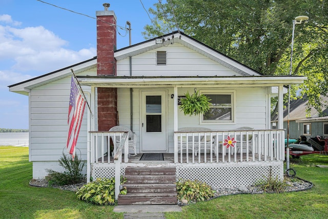 view of front of home with a chimney, covered porch, and a front lawn