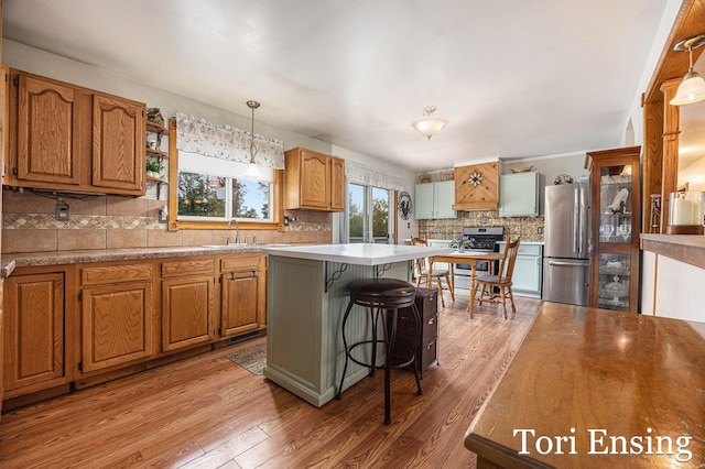 kitchen with a breakfast bar area, decorative backsplash, light wood-style flooring, appliances with stainless steel finishes, and a sink