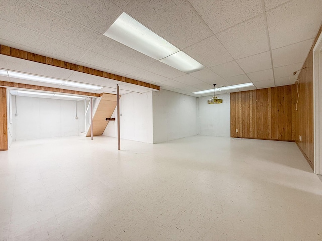 basement featuring a paneled ceiling and wooden walls