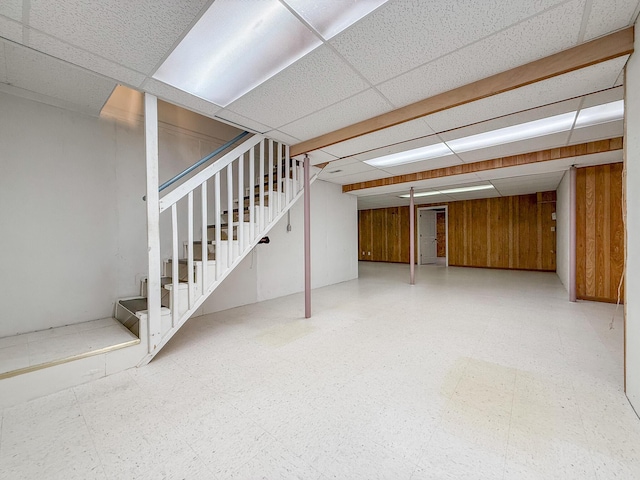 basement featuring a drop ceiling and wooden walls