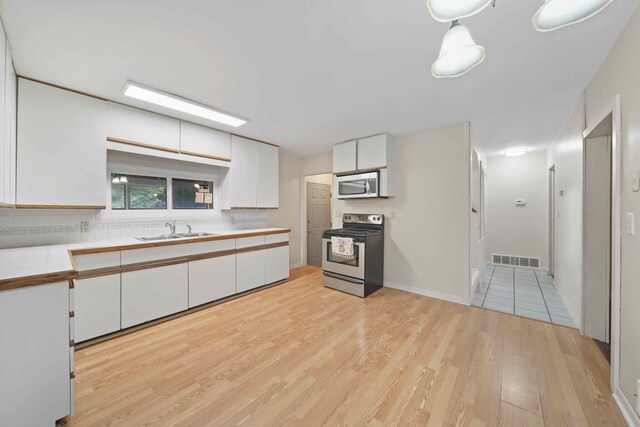 kitchen with tile counters, sink, appliances with stainless steel finishes, white cabinets, and light hardwood / wood-style floors