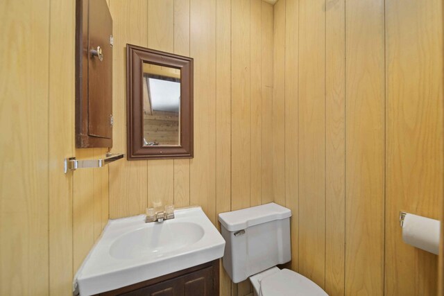 bathroom with vanity, toilet, and wood walls