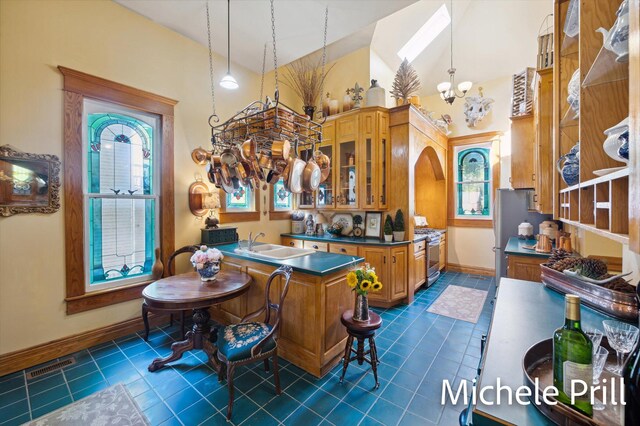 kitchen with stainless steel range with gas stovetop, dark tile patterned flooring, kitchen peninsula, an inviting chandelier, and sink