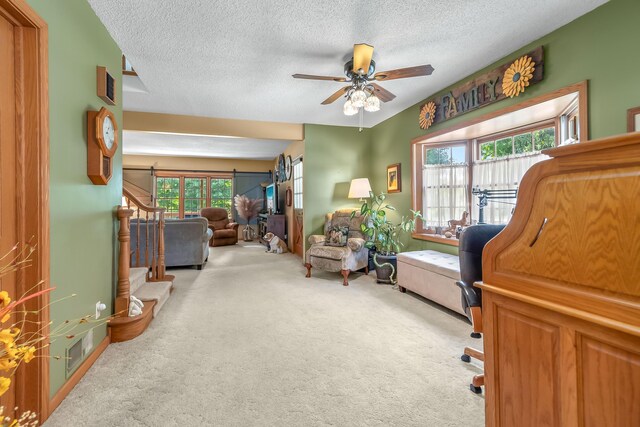 living area featuring ceiling fan, light carpet, and a textured ceiling