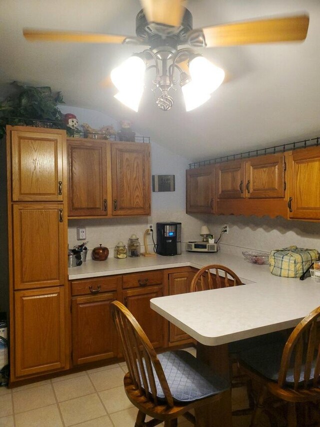 kitchen featuring light tile patterned floors, kitchen peninsula, ceiling fan, a breakfast bar, and vaulted ceiling