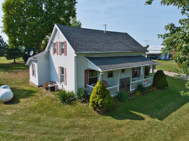 rear view of house featuring central air condition unit, a lawn, and covered porch