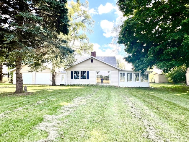 view of front of house with an attached garage, a chimney, a front lawn, and a sunroom