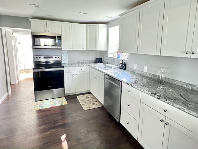 kitchen featuring a sink, light stone counters, dark wood-style floors, appliances with stainless steel finishes, and white cabinets