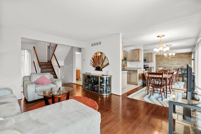 living room with visible vents, an inviting chandelier, light wood-style flooring, and stairway