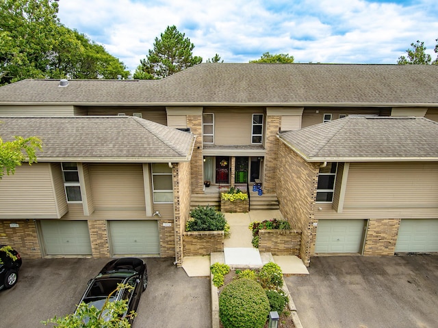 townhome / multi-family property with an attached garage, brick siding, driveway, and roof with shingles