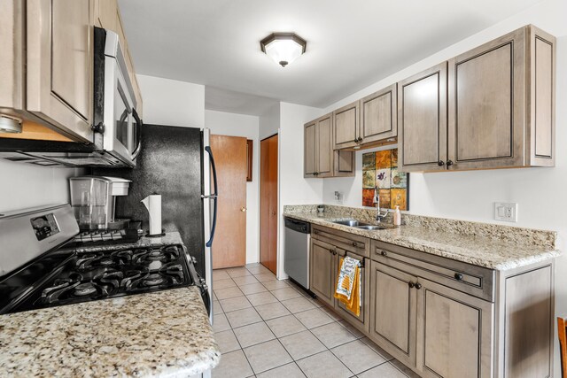 kitchen with light tile patterned floors, black range oven, stainless steel dishwasher, sink, and light stone counters