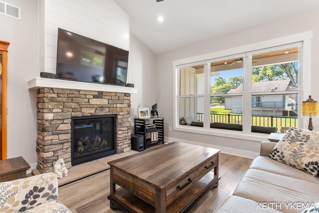 living room with wood-type flooring, a stone fireplace, and vaulted ceiling