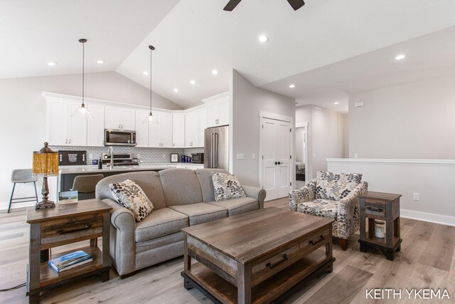 living room with ceiling fan, light hardwood / wood-style flooring, and vaulted ceiling