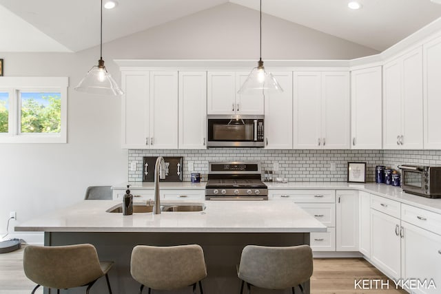 kitchen featuring lofted ceiling, decorative light fixtures, white cabinetry, appliances with stainless steel finishes, and decorative backsplash