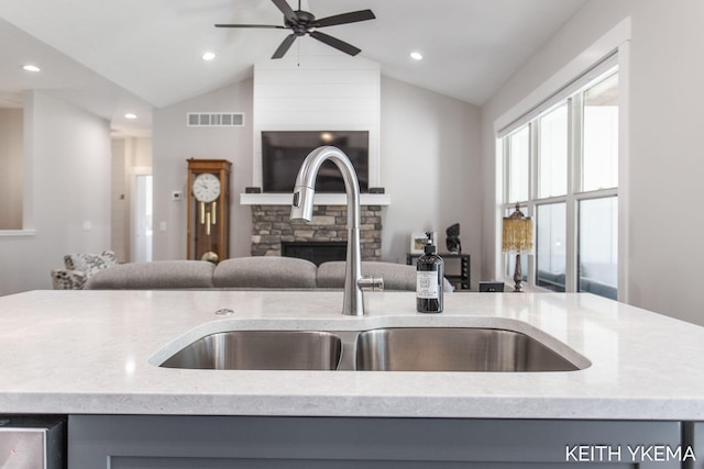 kitchen featuring vaulted ceiling, ceiling fan, sink, and a stone fireplace