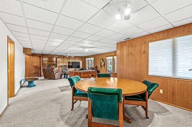 dining area with wooden walls, a drop ceiling, and carpet