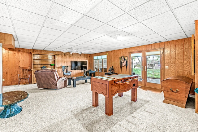 game room with light colored carpet, a drop ceiling, and wood walls