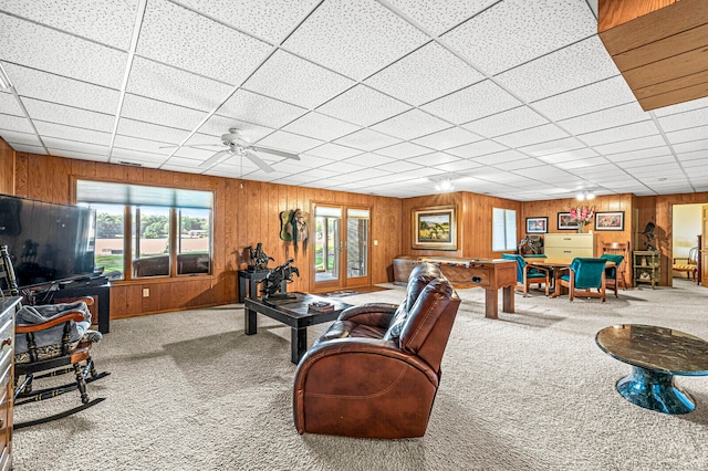 carpeted living room with a drop ceiling, wood walls, and ceiling fan