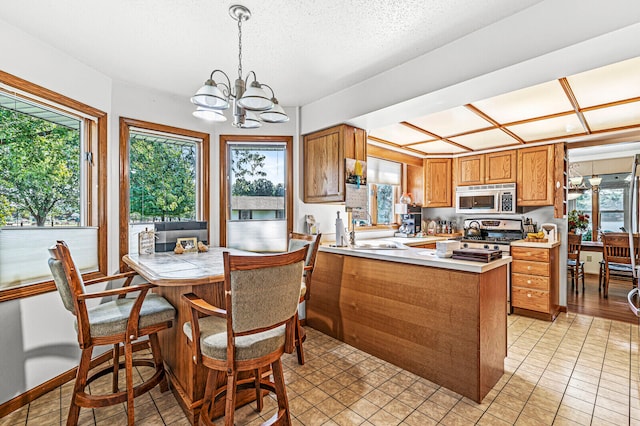 kitchen with hanging light fixtures, kitchen peninsula, stainless steel appliances, and plenty of natural light