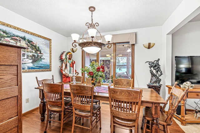 dining space with wood-type flooring, a textured ceiling, and a chandelier