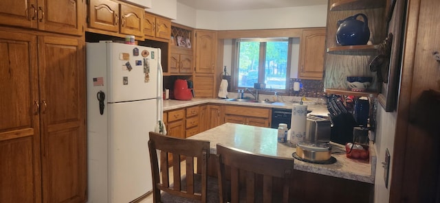 kitchen with light countertops, decorative backsplash, freestanding refrigerator, brown cabinetry, and a sink