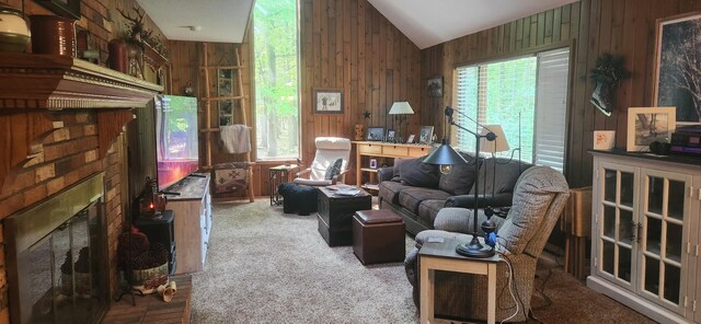 carpeted living room with lofted ceiling, a brick fireplace, a healthy amount of sunlight, and wooden walls