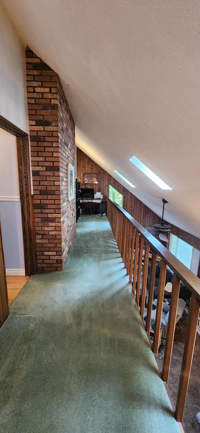 stairway with wood walls, a fireplace, lofted ceiling with skylight, carpet, and ceiling fan