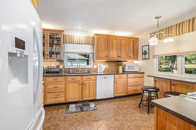 kitchen featuring white appliances, pendant lighting, tasteful backsplash, sink, and a chandelier