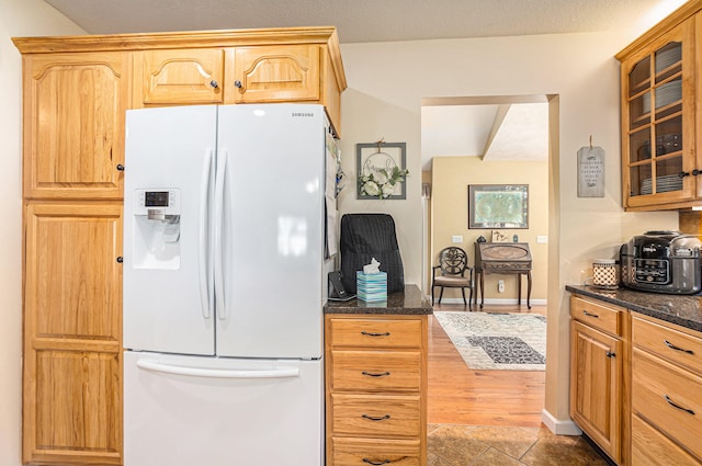 kitchen featuring dark stone countertops, hardwood / wood-style flooring, and white fridge with ice dispenser