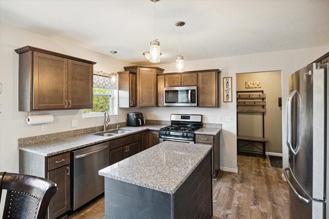 kitchen with appliances with stainless steel finishes, dark wood-type flooring, sink, decorative light fixtures, and a center island