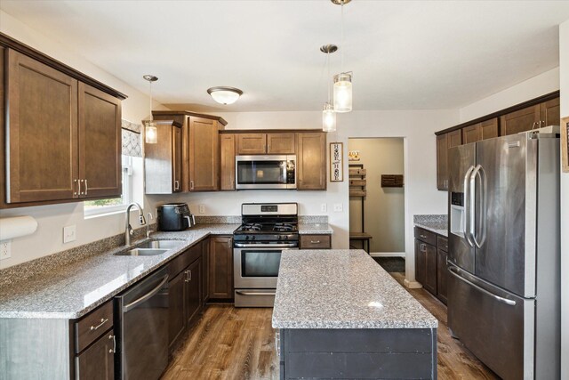 kitchen featuring pendant lighting, sink, dark hardwood / wood-style floors, light stone countertops, and appliances with stainless steel finishes