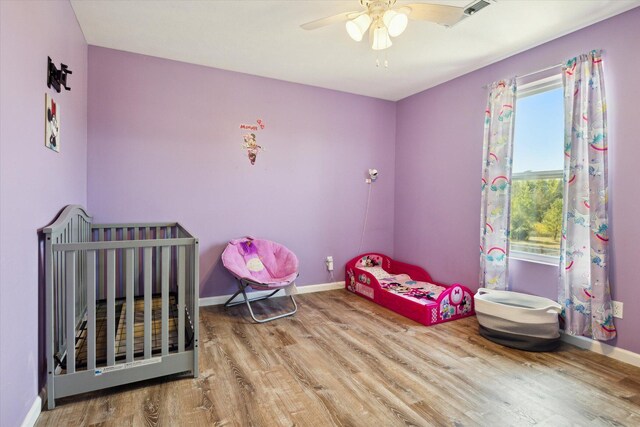 bedroom with hardwood / wood-style flooring, a nursery area, and ceiling fan