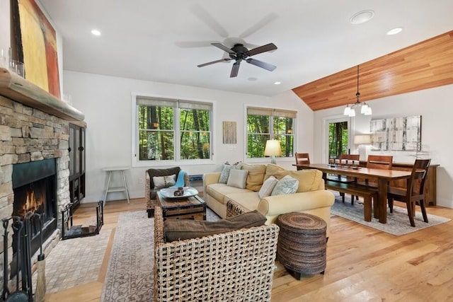 living room with ceiling fan with notable chandelier, lofted ceiling, a fireplace, and light hardwood / wood-style flooring