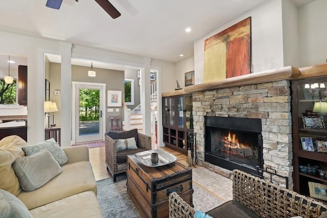 living room featuring ceiling fan, a stone fireplace, and wood-type flooring