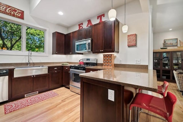 kitchen featuring sink, hanging light fixtures, appliances with stainless steel finishes, light hardwood / wood-style floors, and kitchen peninsula