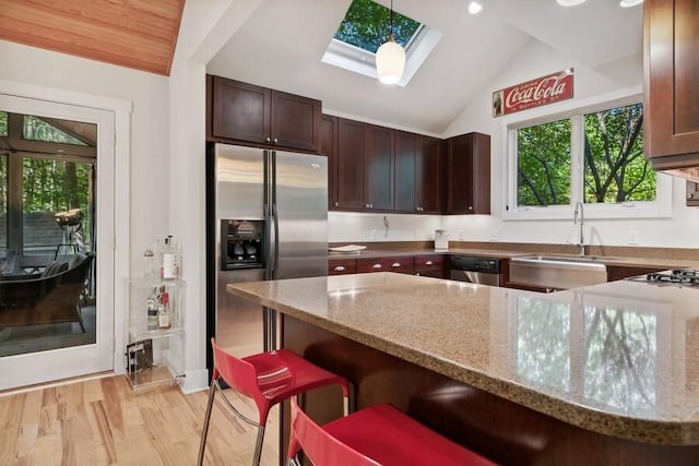 kitchen with light stone countertops, hanging light fixtures, stainless steel appliances, lofted ceiling with skylight, and a kitchen bar