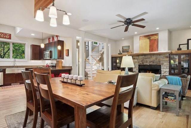 dining area with ceiling fan, sink, light wood-type flooring, and a fireplace