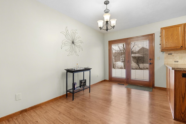 doorway to outside with light hardwood / wood-style flooring and an inviting chandelier