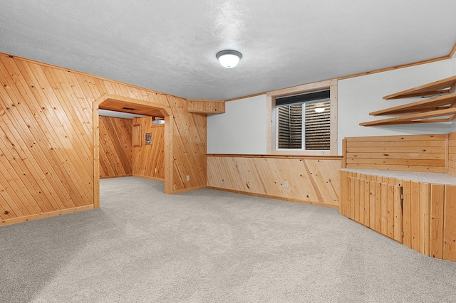 interior space featuring a textured ceiling, crown molding, light carpet, and wooden walls