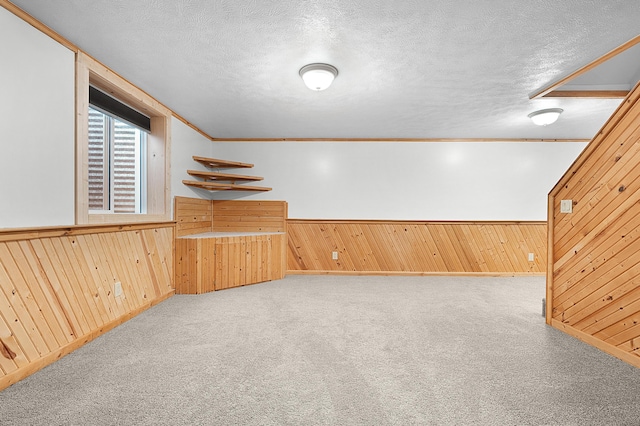 basement with a textured ceiling, light colored carpet, and wood walls