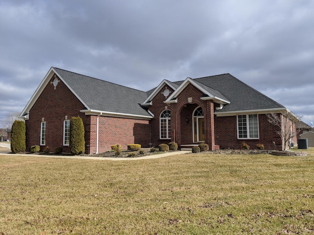 traditional home with a front yard, central AC unit, brick siding, and a shingled roof