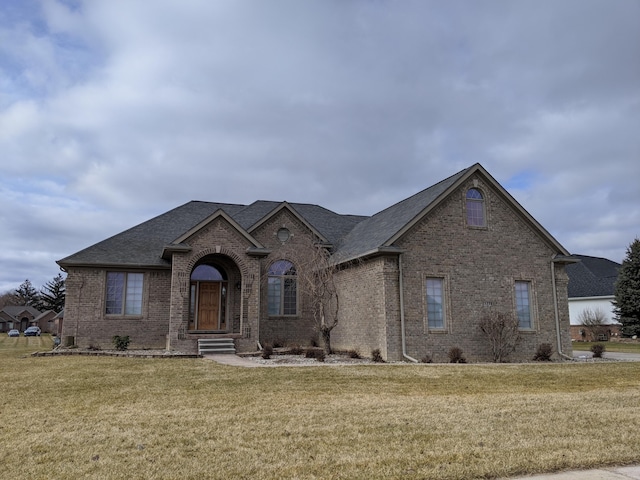 view of front of property featuring brick siding, a front lawn, and roof with shingles