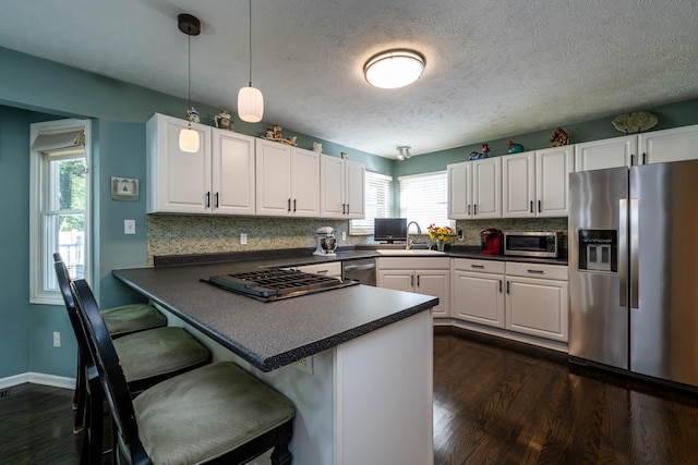 kitchen featuring white cabinets, sink, kitchen peninsula, appliances with stainless steel finishes, and decorative light fixtures