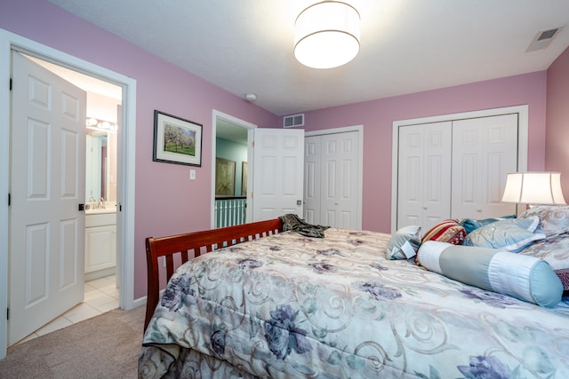 carpeted bedroom with ensuite bathroom, multiple closets, and sink