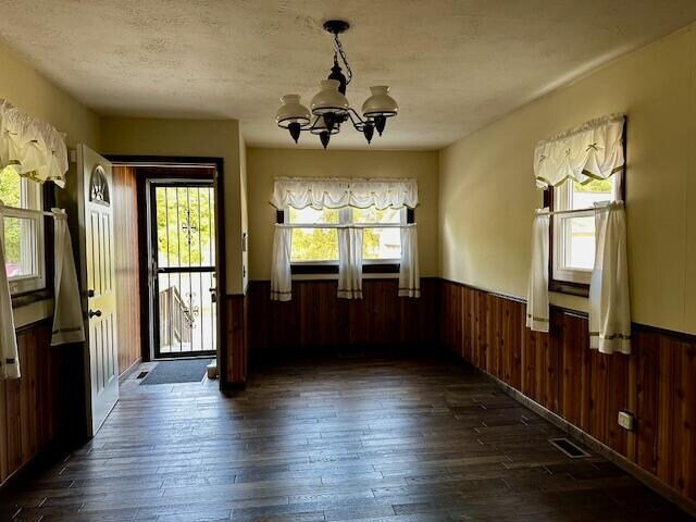 entrance foyer featuring a textured ceiling, wood walls, an inviting chandelier, and dark hardwood / wood-style flooring