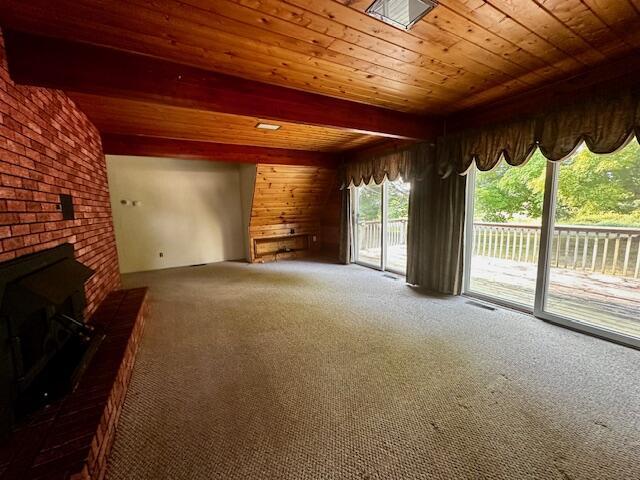 unfurnished living room with a skylight, wooden ceiling, a brick fireplace, carpet flooring, and beamed ceiling