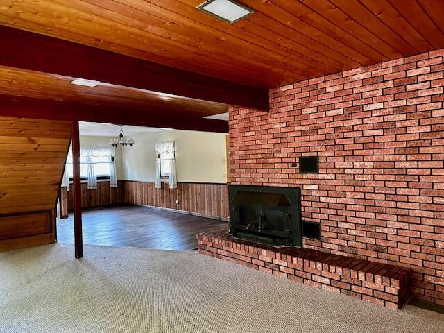 unfurnished living room with beamed ceiling, wood walls, a brick fireplace, hardwood / wood-style flooring, and brick wall