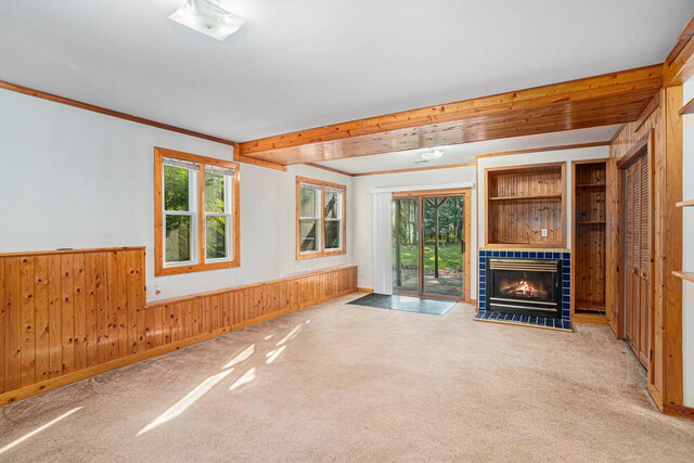 unfurnished living room featuring a tiled fireplace, carpet, ornamental molding, and wooden walls