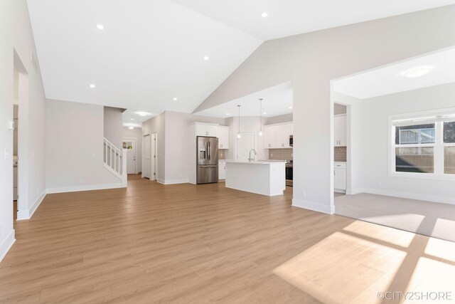 unfurnished living room with light wood-type flooring, lofted ceiling, and sink